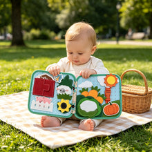 Load image into Gallery viewer, Mes Premiers Animaux de la Ferme - Livre bébé : bébé joue avec son livre pendant un pique-nique au parc
